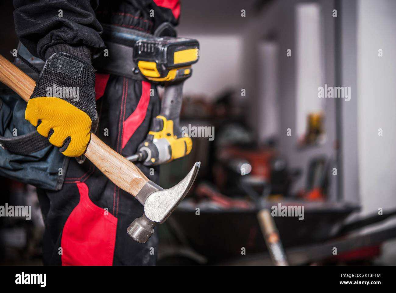 Closeup of Construction Worker Holding a Hammer in His Right Hand. Electric Screwdriver Hanging on a Tool Belt in the Background. Professional Buildin Stock Photo