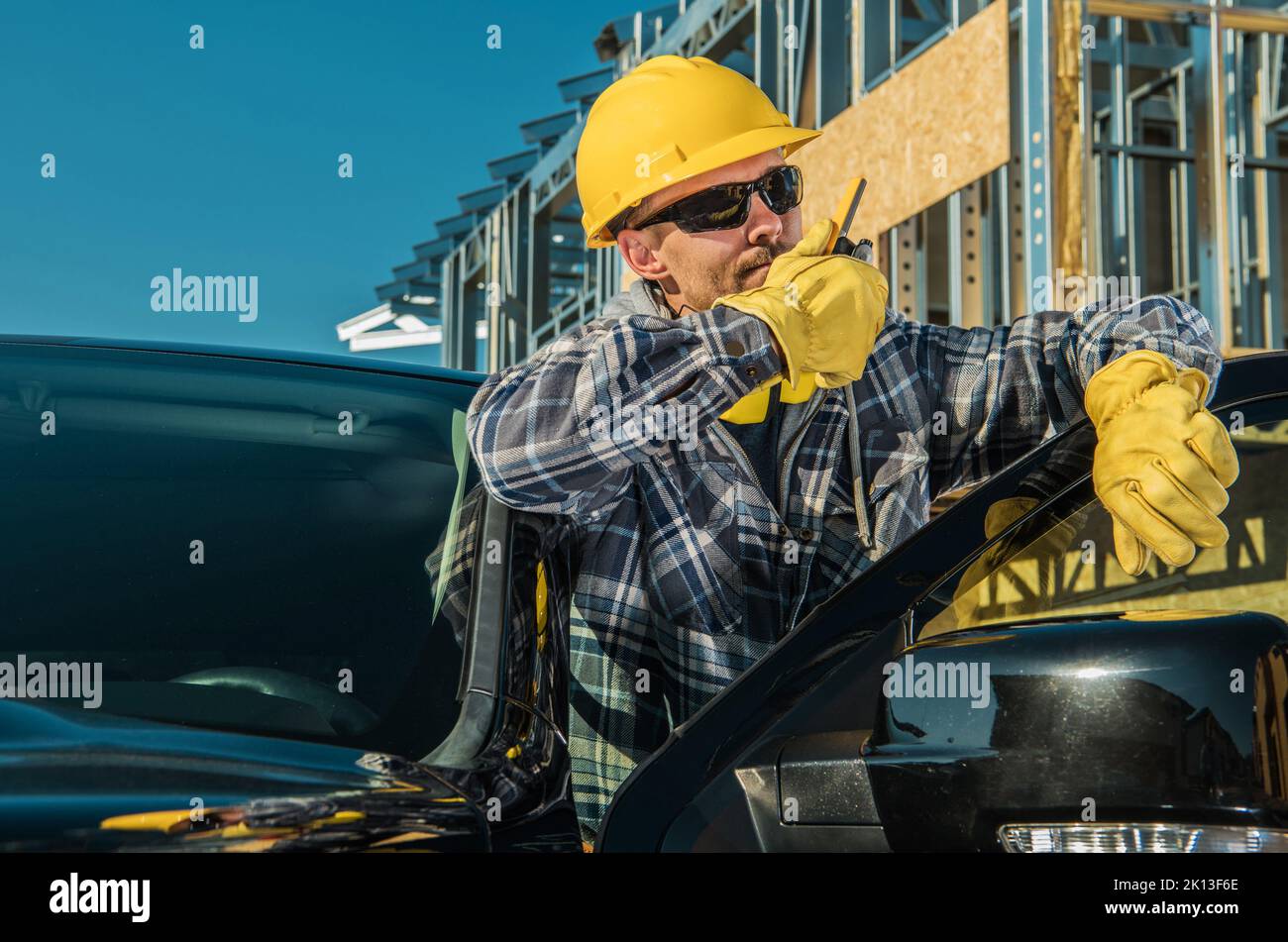 Caucasian Middle Aged Man Standing Next to His Pickup Truck Communicating with Other Workers Using Citizens' Band Radio Transmitter. Construction Supe Stock Photo