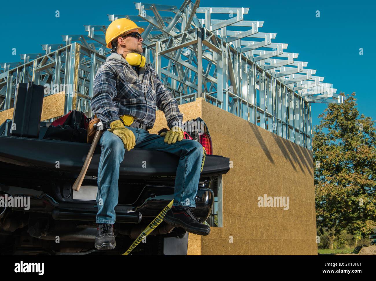 Caucasian Middle Aged Contractor Proudly Sitting on the Front Panel of His Pickup Truck Cargo Bed. Tools are Packed in the Trunk After Finished Day at Stock Photo