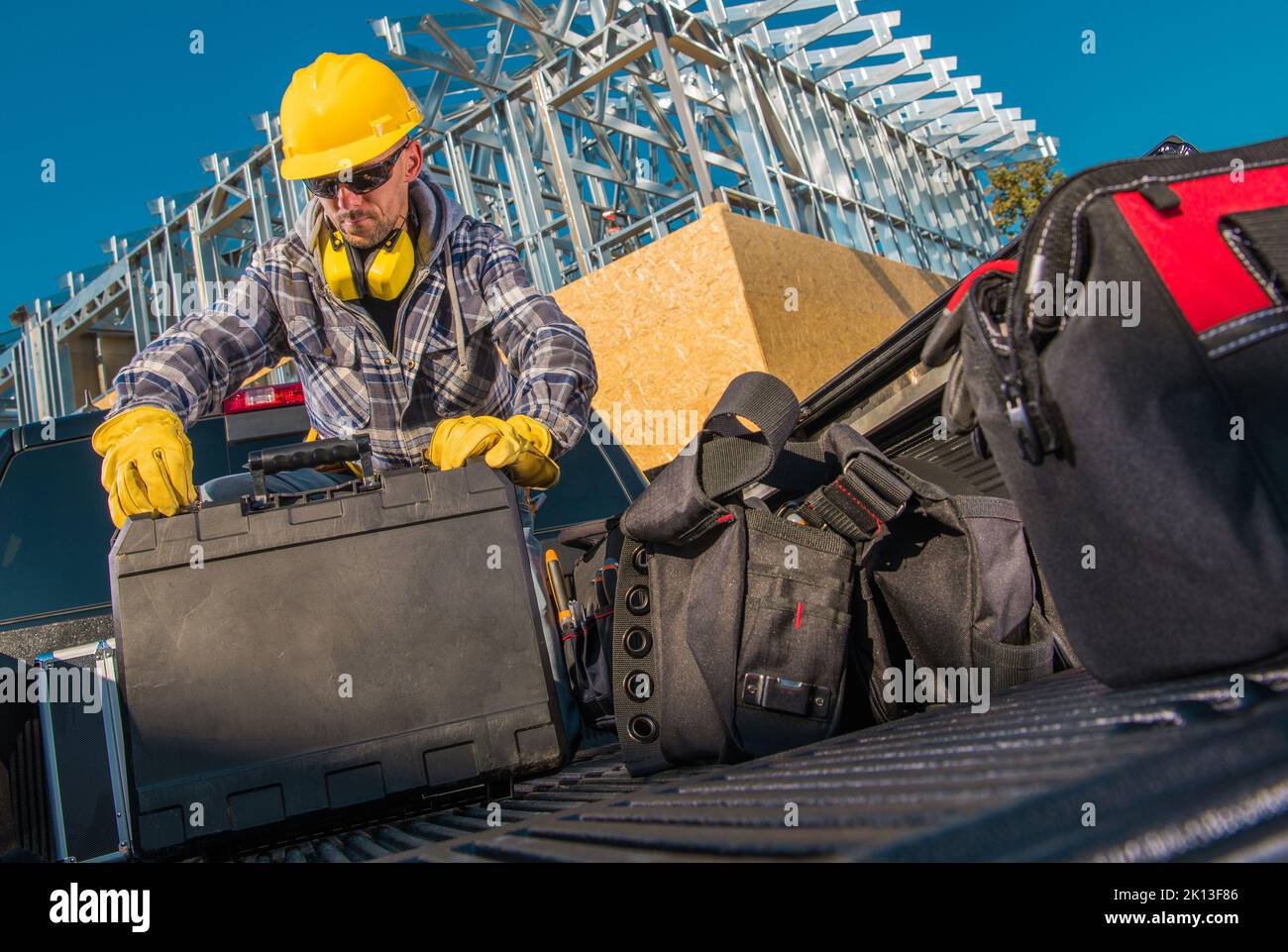 Caucasian Middle Aged Construction Worker Packing His Professional Equipment and Working Tools Into the Cargo Beg of Black Pickup Truck. Residential B Stock Photo