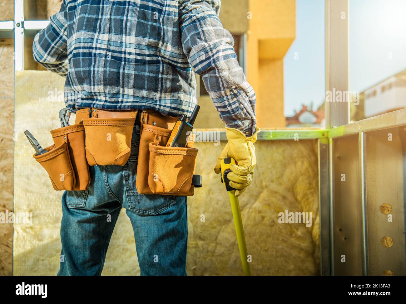 Rear View Photo of Professional Carpentry Worker with a Tape Measure Estimating Spacing Between Steel Parts of thee Building Structure to Prepare Timb Stock Photo