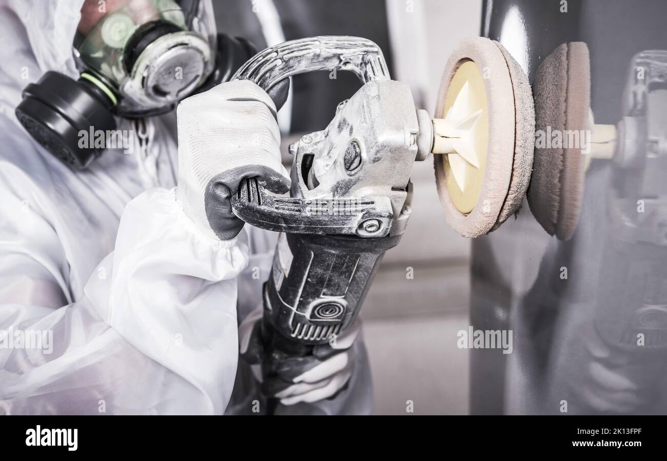 Car Detailing Studio Worker in White Protective Coverall and Full Face Mask Polishing Vehicle Paint Varnish with Electric Polisher Tool. Automotive Th Stock Photo