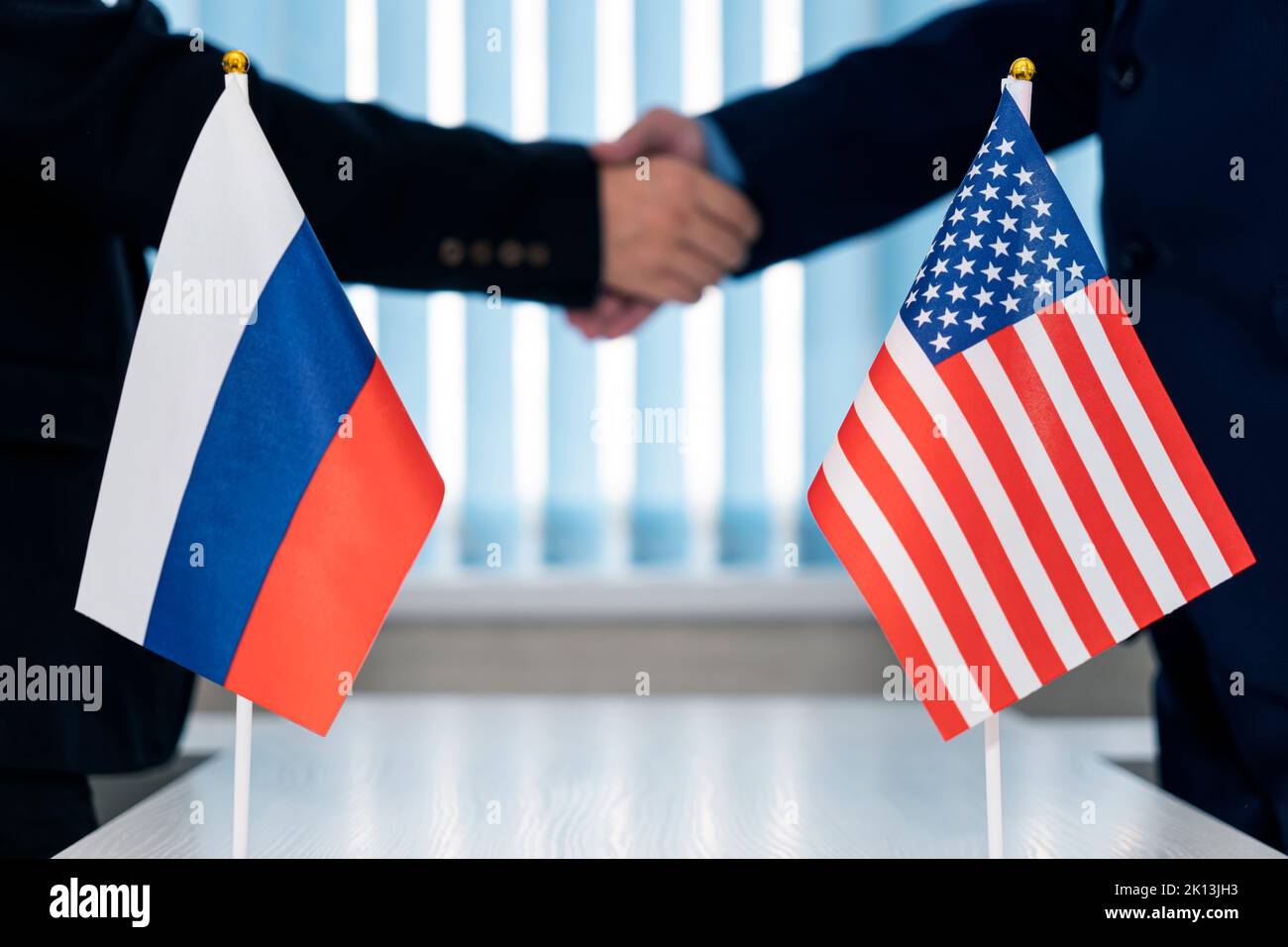 Close-up Of Two Businesspeople Shaking Hands In Front Of Us Russia Flags On Table Stock Photo