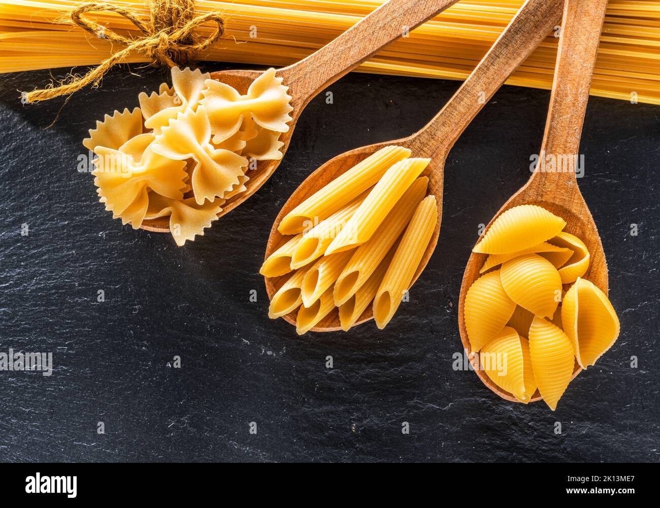 Assortment of pasta in wooden spoons on black background. Top view. Stock Photo
