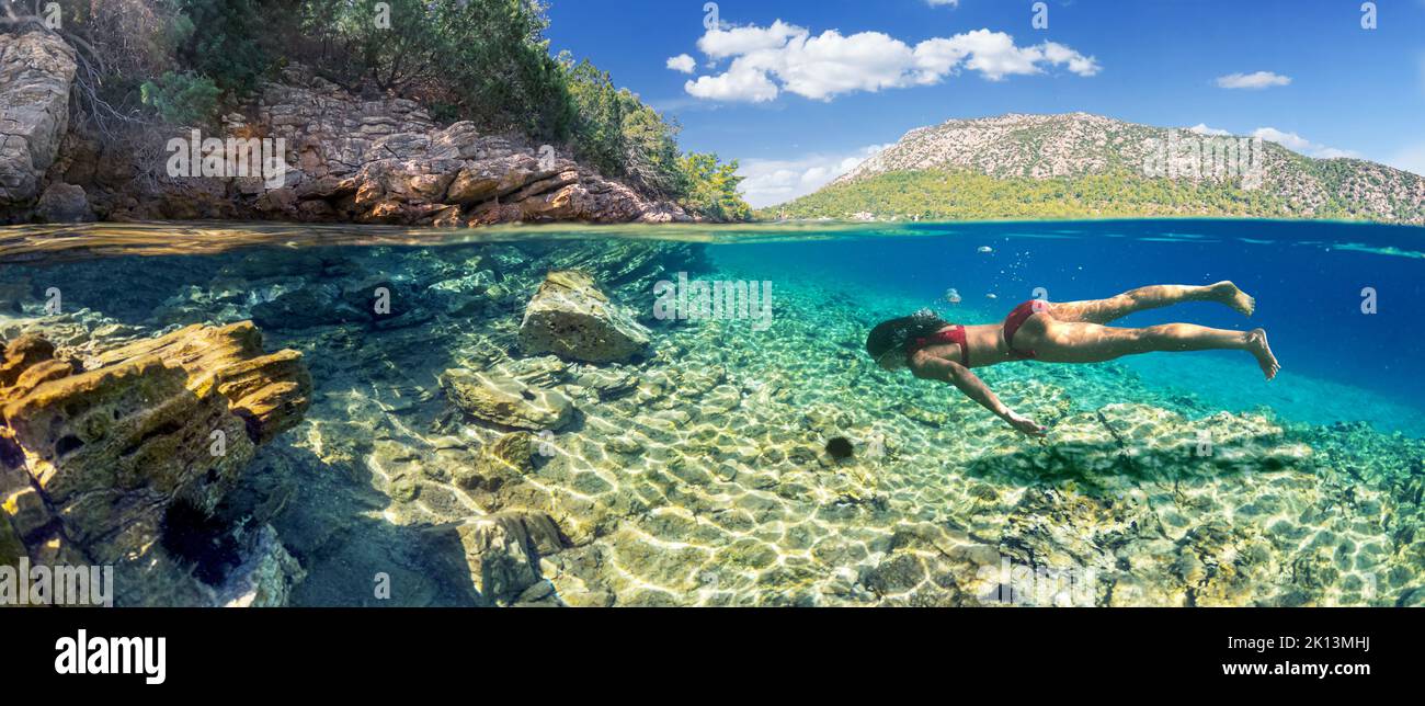 Woman diver is snorkeling on a beautiful sea beach. The lower half of the image is occupied by the seabed, the upper half by the coast and the sky. Stock Photo