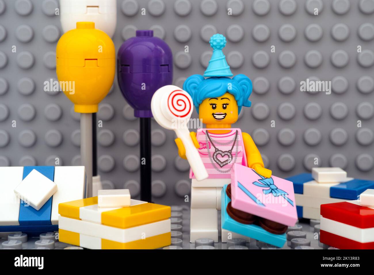 Tambov, Russian Federation - January 17, 2021 A Lego birthday girl minifigure with lollipop, gifts, balloons against a gray baseplate background Stock Photo