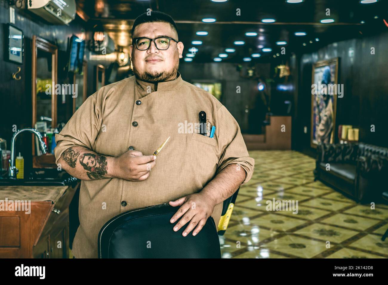 Fat barber with glasses looks at camera and holds scissors. Vintage barber shop Stock Photo