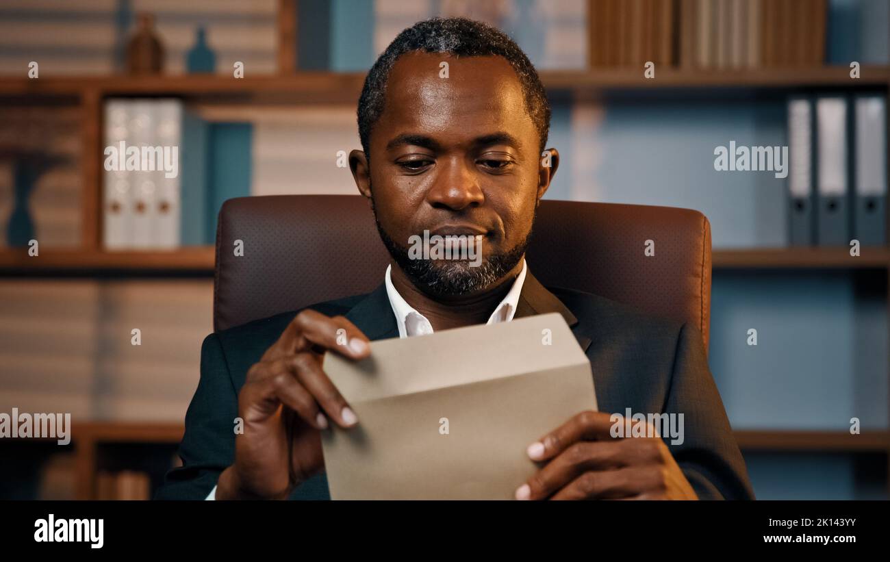 Successful businessman sits in office opening paper envelope reading letter with good news received bank loan approval profitable proposition happy Stock Photo