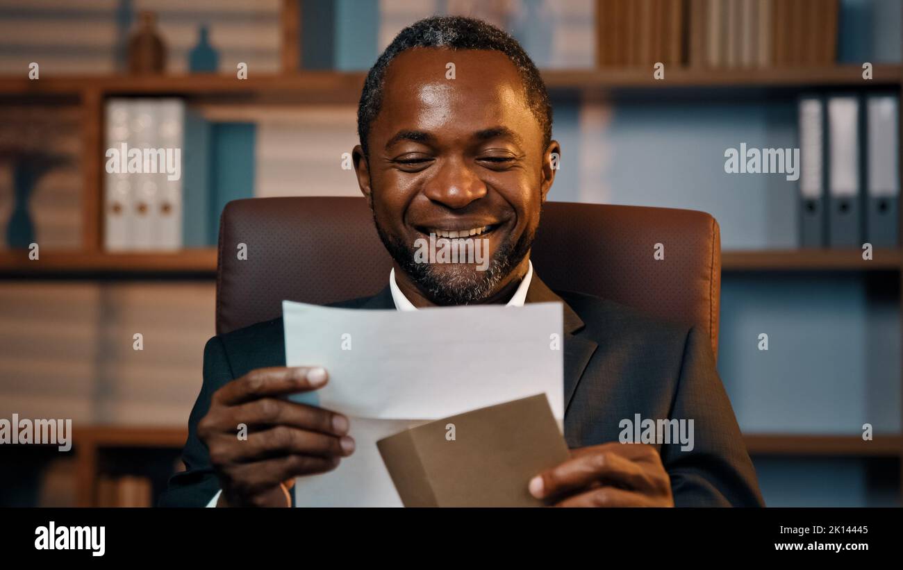 Successful businessman sits in office opening paper envelope reading letter with good news received bank loan approval profitable proposition happy Stock Photo