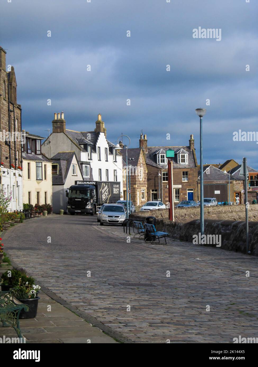 Cobblestone road in the morning, at the harbor of the small Scottish fishing village of Stonehaven, with ominous steel blue clouds in the background. Stock Photo