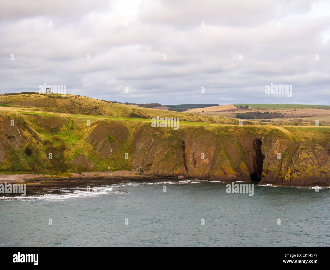 The steep basalt cliffs of the northern Scottish coastline, with a memorial on the Horizon, Stock Photo