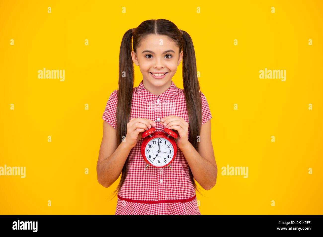 Teenager child hold clock isolated on yellow studio background