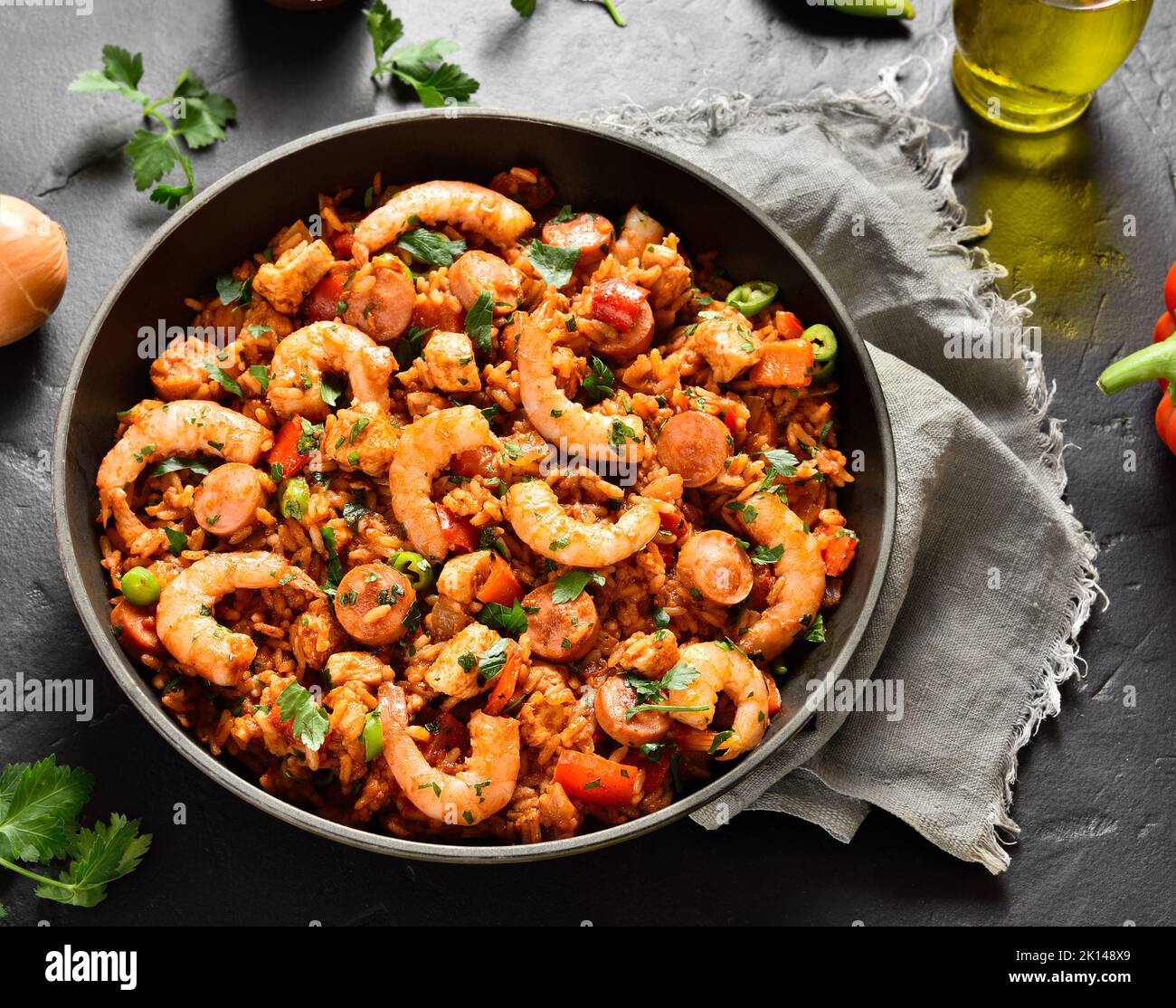 Creole style jambalaya with chicken, smoked sausages and vegetables in frying pan over black stone background. Close up view Stock Photo