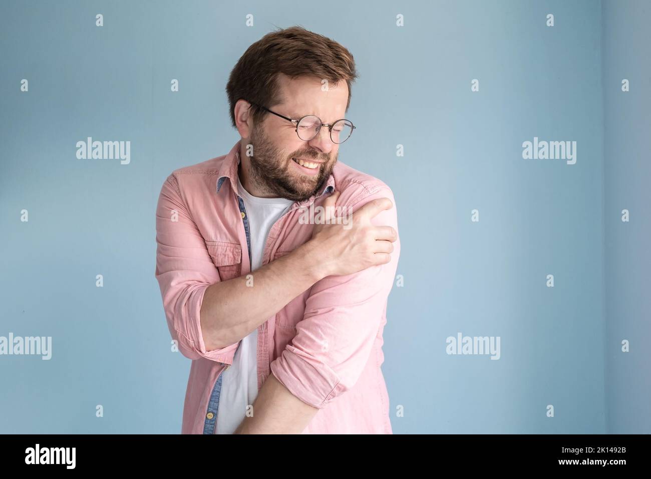 Man is experiencing severe pain in shoulder, he is suffering, made a painful grimace and put hand on the sore spot. Medical concept.  Stock Photo