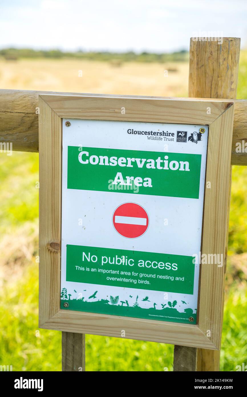 Conservation sign on a wooden fence in front of a field with a blue summer sky background. Stock Photo