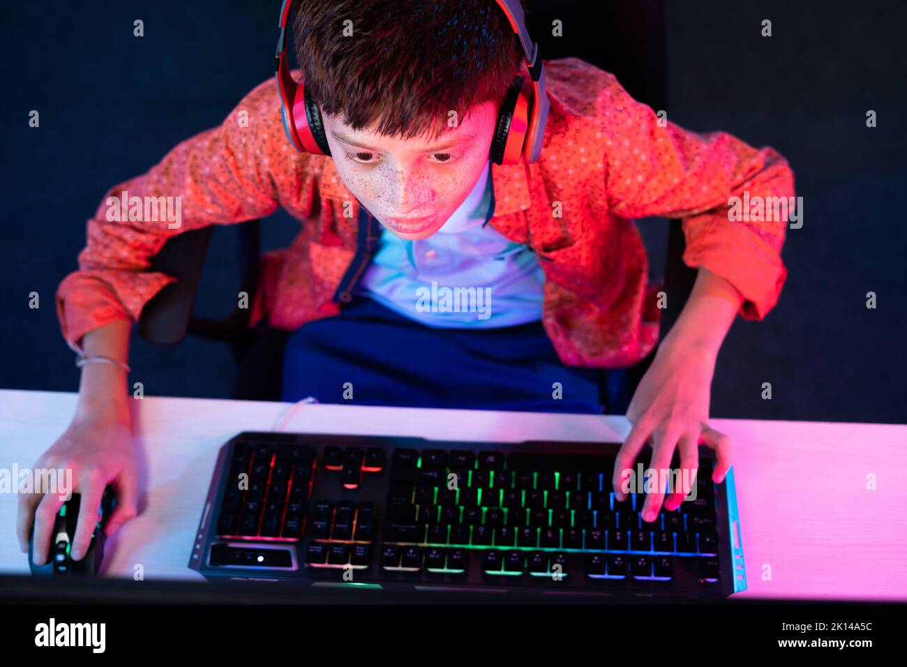 focus on kid, Top view shot of teenager kid with headphones playing video game on computer by using keyboard at home - concept of entertainment Stock Photo
