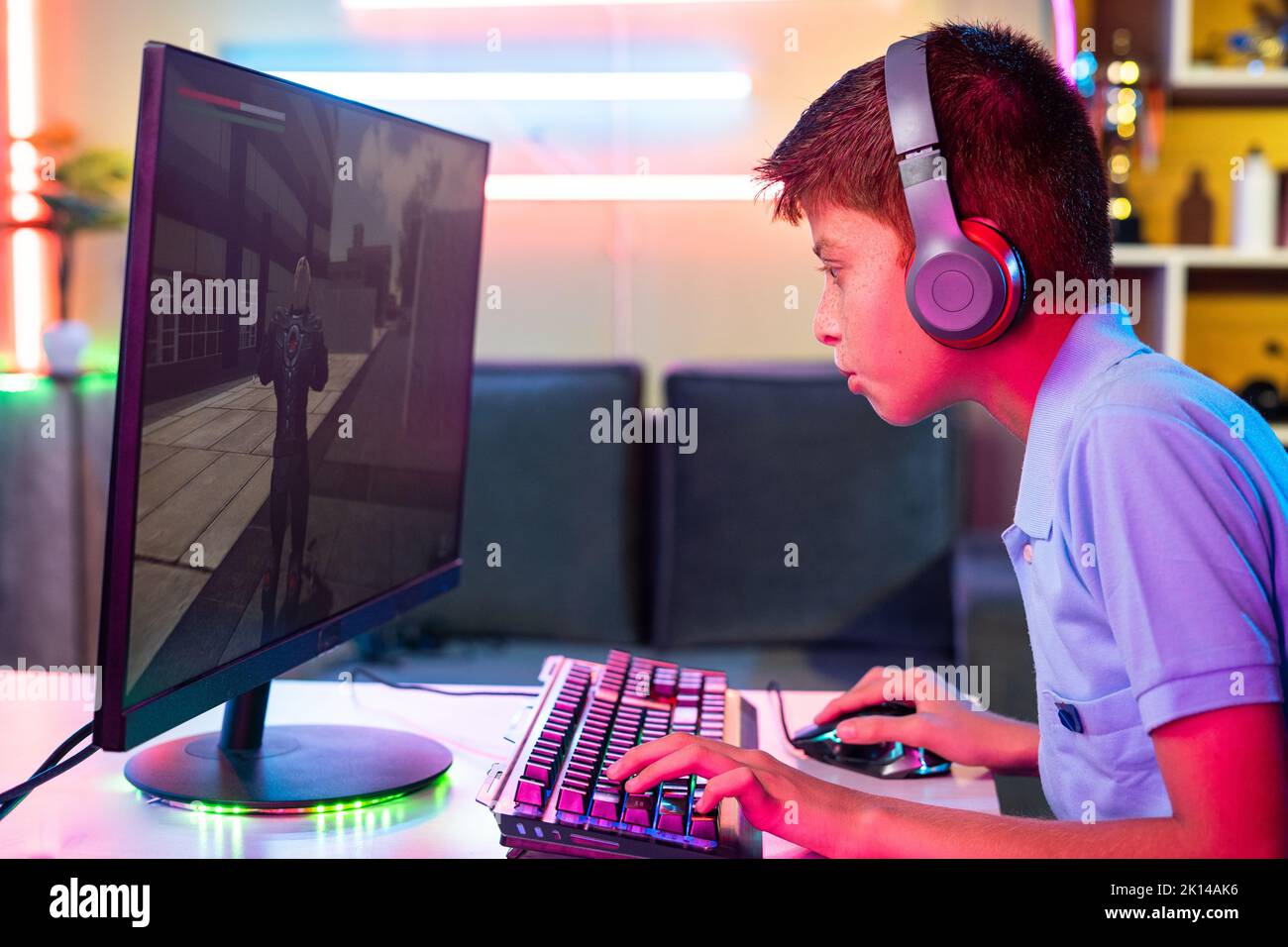 side view of teenager kid with headphones playing online video game on computer at home - concept of competitive, leisure activity and game addiction. Stock Photo