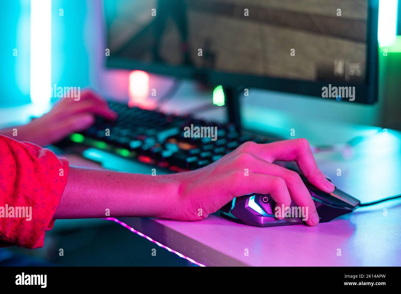 Close up shot of teenager kid hands using mouse while playing video game at neon light background - concept of entertainment, hobbies and technology. Stock Photo