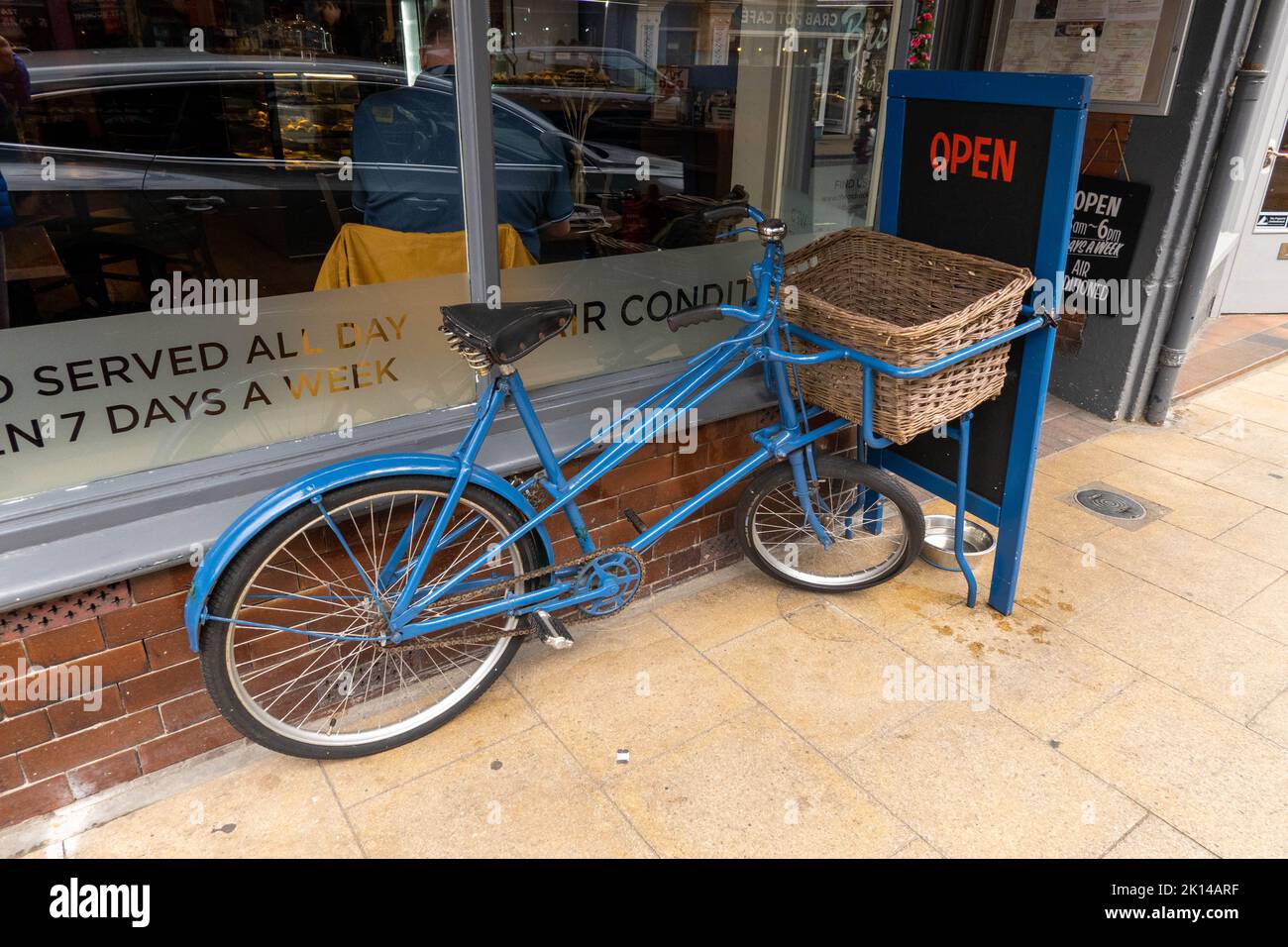 An old butchers delivery trade bike with wicker basket on front standing next to a cafe in Cromer Norfolk Stock Photo