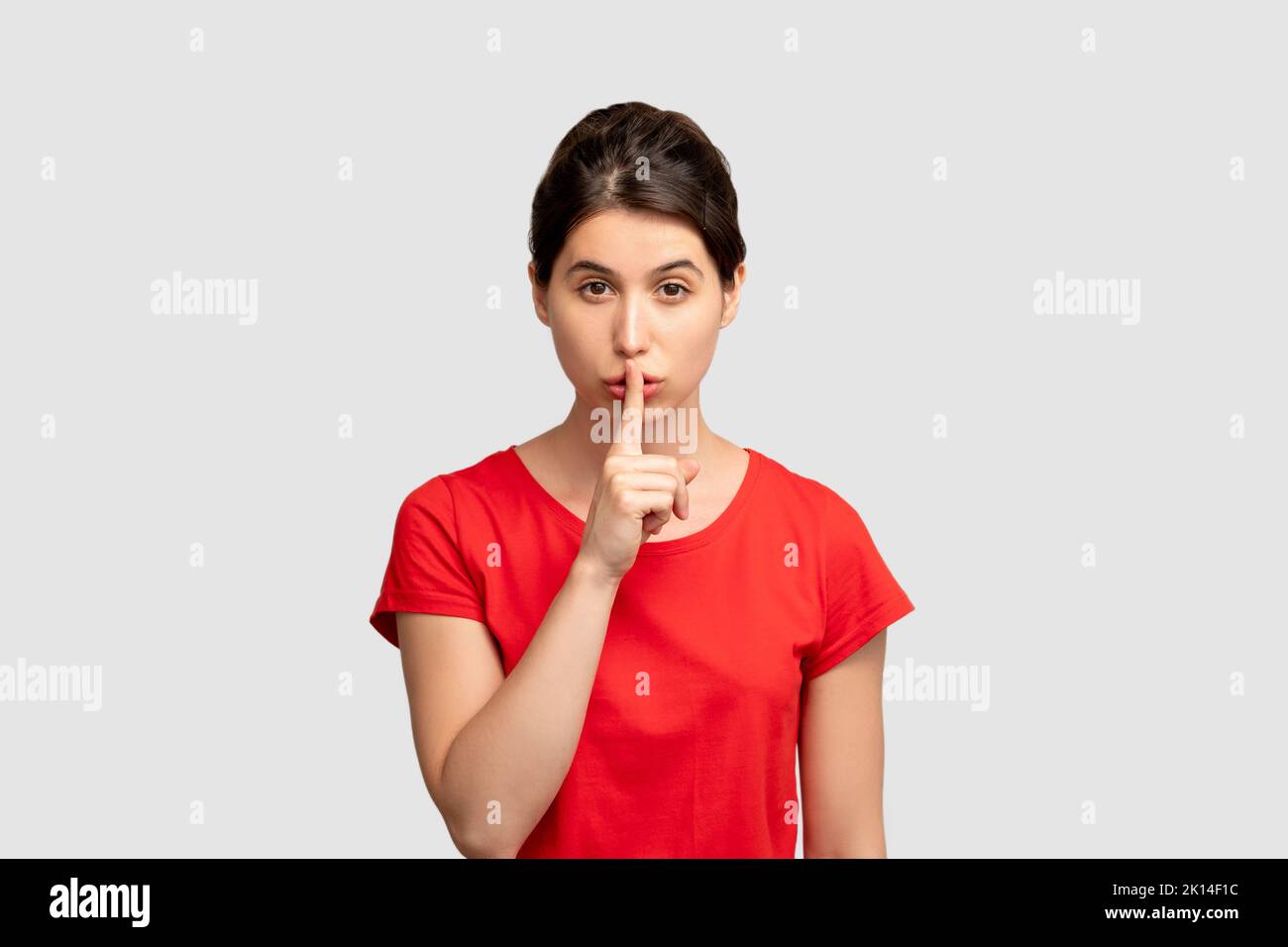 Silence gesture. Keep secret. Woman putting finger on mouth. Looking at camera isolated on neutral copy space. Asking be quite. No word. Advertising b Stock Photo