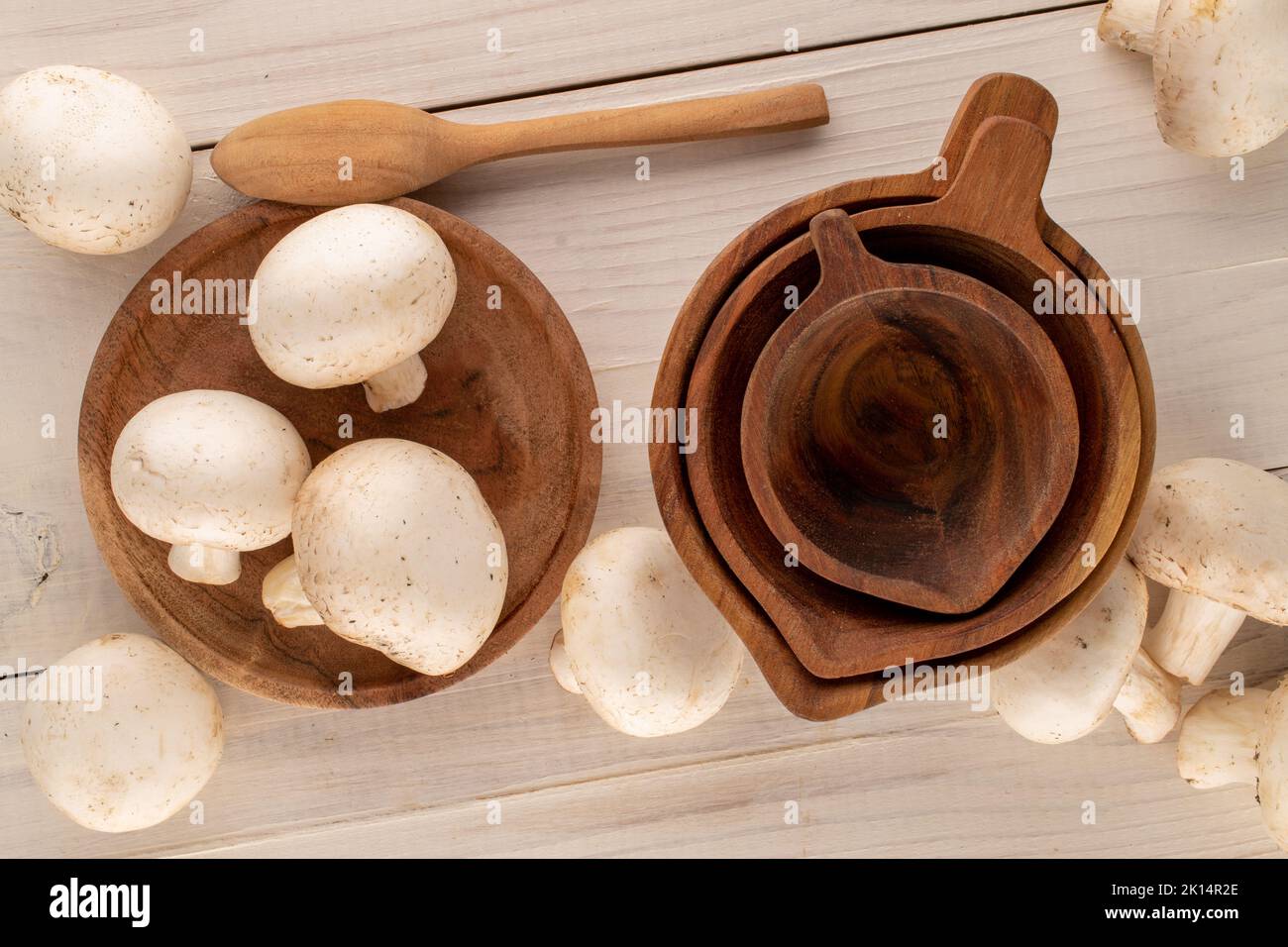 Several fresh organic mushrooms with wooden utensils on a wooden table, close-up, top view. Stock Photo