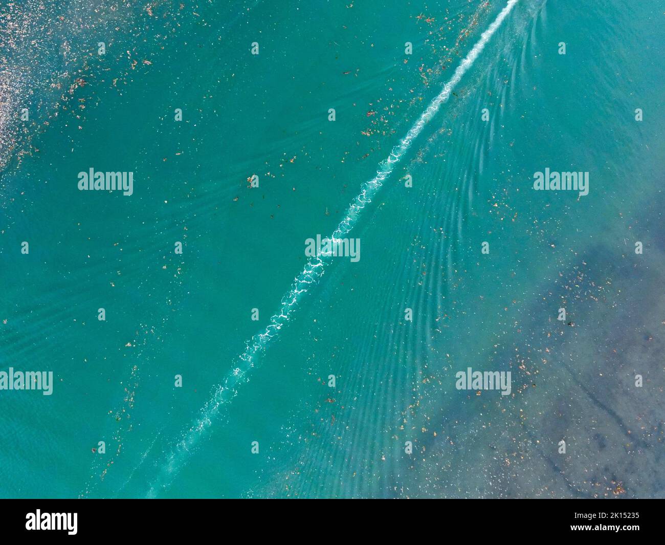 Aerial view of the pattern made on water by the wake of a speedboct as it passed through floating debris in an estuary. No people. Stock Photo