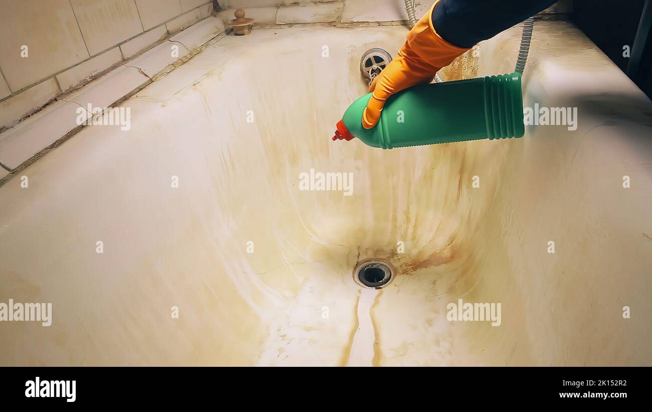 Male hand in orange rubber gloves pours a gel into the sink to clean or wash the tub and toilet in the bathroom.  Stock Photo