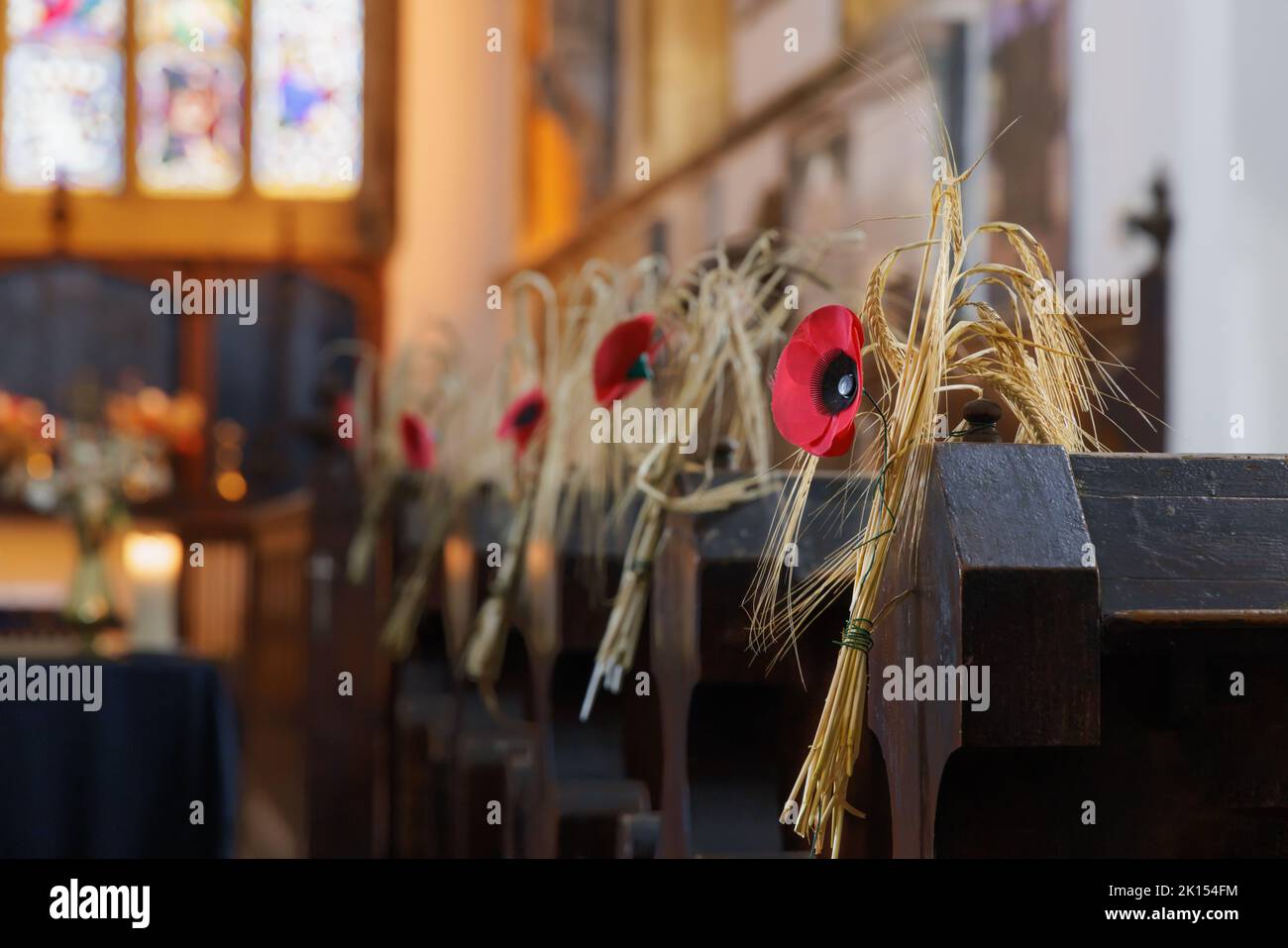 Traditional corn dollies decorated with poppies are affixed to the ends of pews in a Northamptonshire village church for the Harvest Festival. Stock Photo