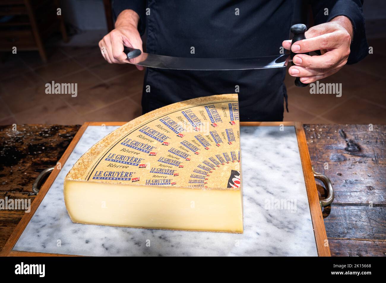 July 11 2022, Lyon, France : A man cuts a portion of The Gruyère with a wire, the famous swiss cheese in a cellar on a marbble background Stock Photo