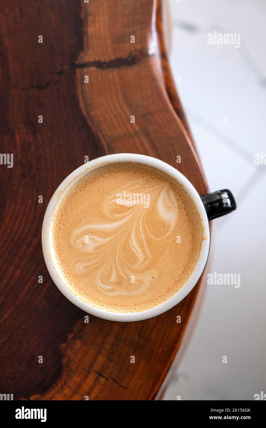 Freshly served cup of cappuccino with latte art on a wooden table in a cafe. Stock Photo