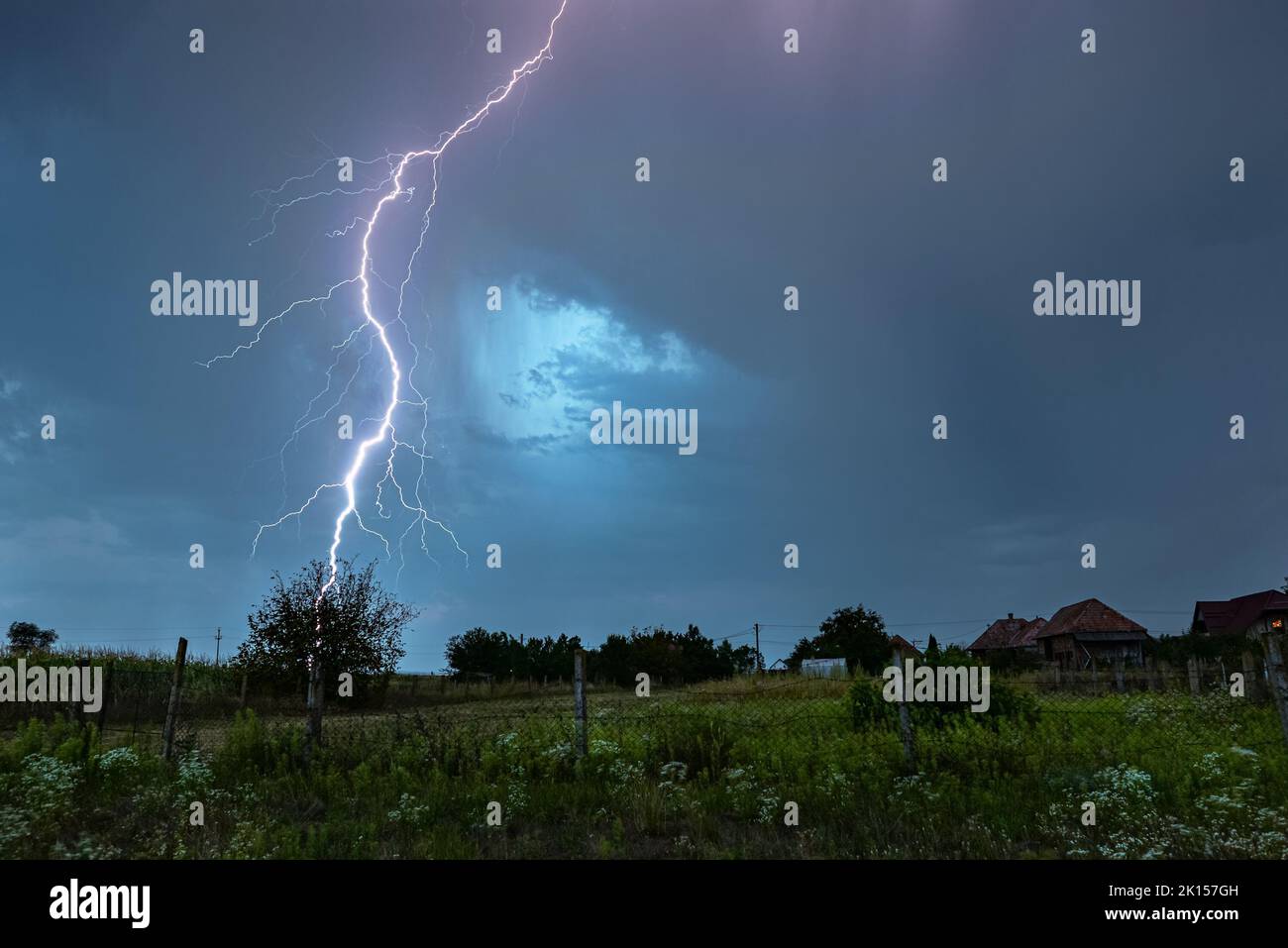 Powerful branched thunderbolt of lightning strikes down in an idyllic countryside Stock Photo