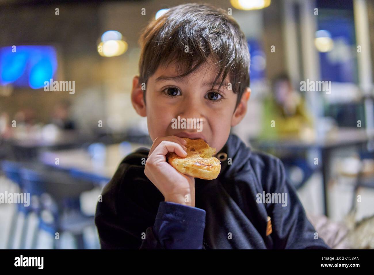 portrait of latin boy looking at the camera eating a crescent roll for breakfast in an argentinian bar. selective focus Stock Photo
