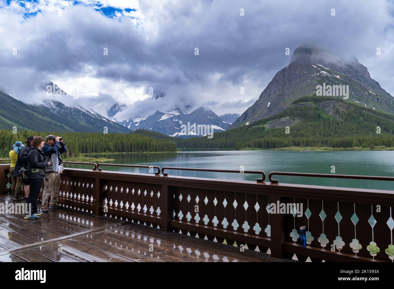 Montana, USA - July 4, 2022: Tourists on the deck of the Many Glacier hotel use binoculars to spot wildlife in Glacier National Park Stock Photo