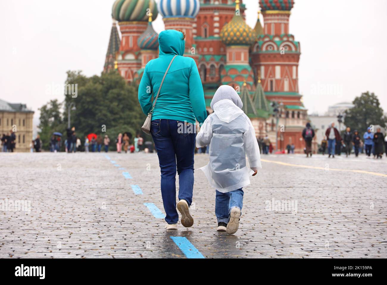 Rain in Moscow, woman with child in raincoat walk on a Red square on background of St. Basil's Cathedral. Rainy weather in autumn Russia Stock Photo