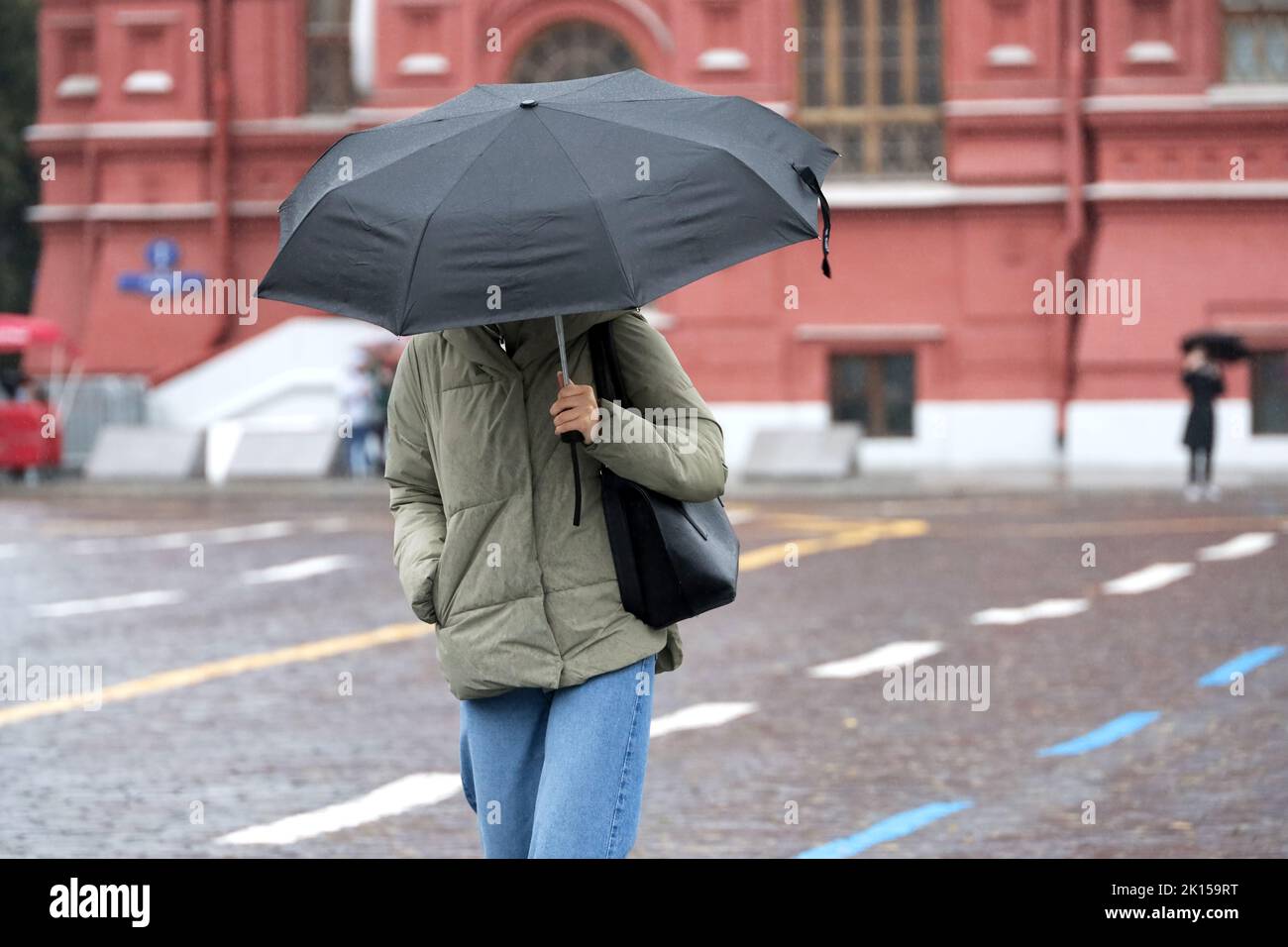 Rain in city, slim girl in jeans and jacket walk with black umbrella on a street. Rainy weather in autumn Stock Photo