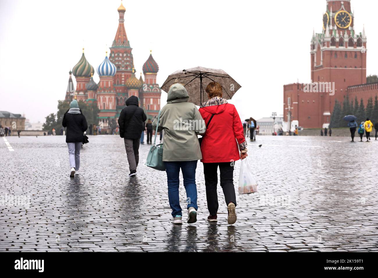 Rain in Moscow, two women with one umbrella walk on a Red square on background of St. Basil's Cathedral and Kremlin tower. Rainy weather in autumn Stock Photo
