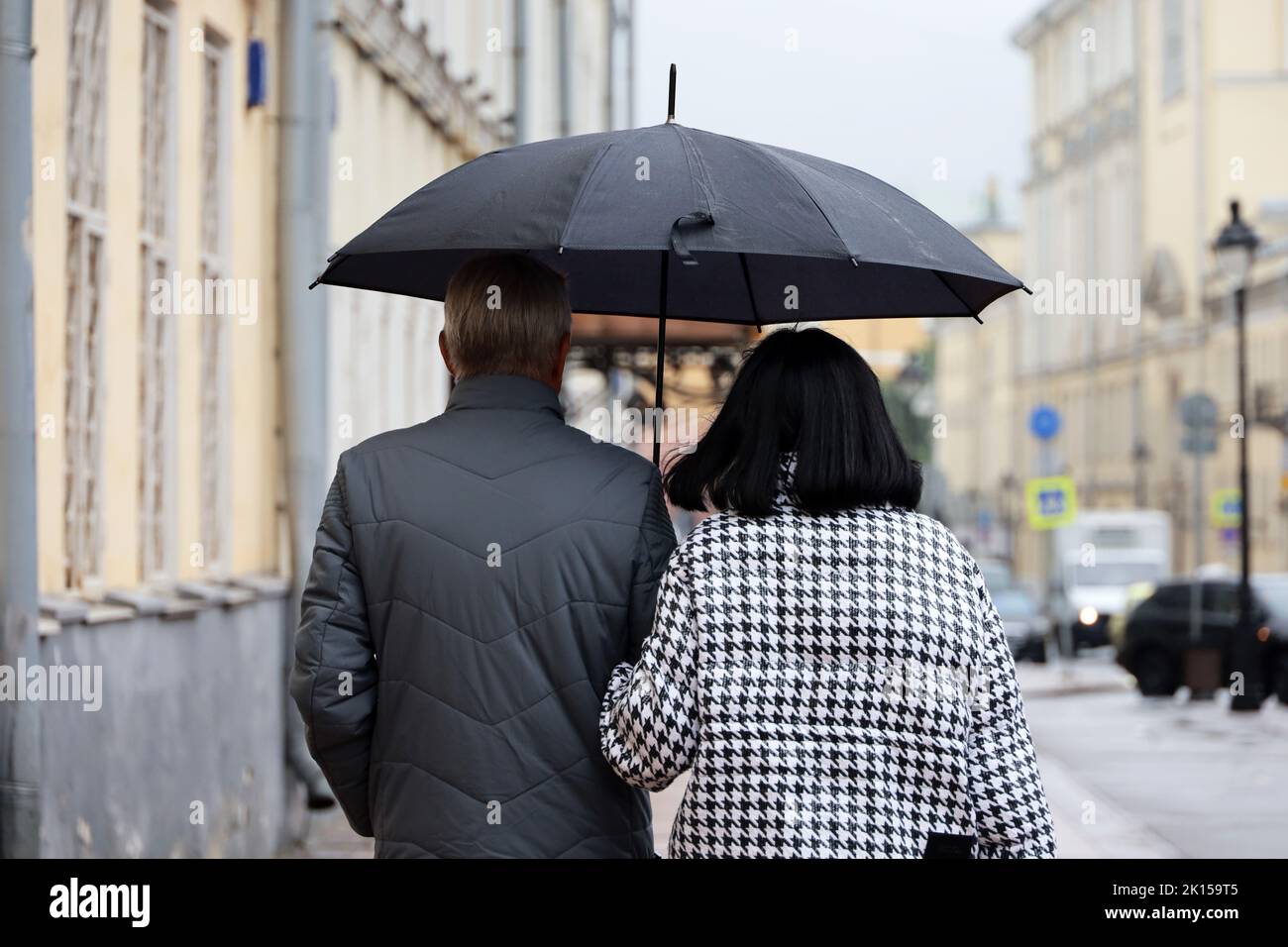 Rain in city, couple with one umbrella walking on a street. Rainy weather in autumn Stock Photo
