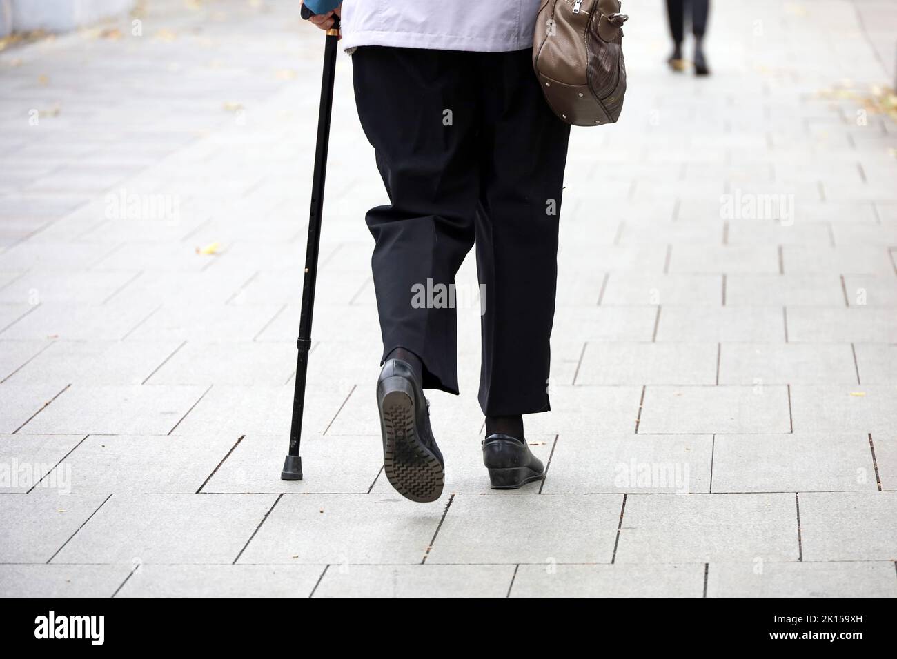 Old woman walking with a cane down the city street. Diseases of the spine and legs of elderly people Stock Photo