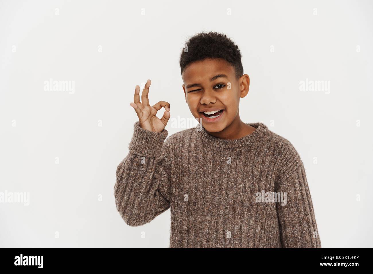 Black preteen boy wearing sweater showing ok gesture and winking isolated over white background Stock Photo