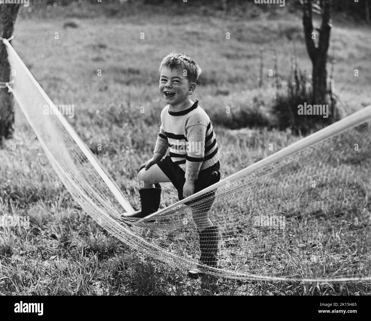 The photograph is captioned: 'What did you expect, Forest Hills?'. A laughing young boy tramples a tennis net. Stock Photo