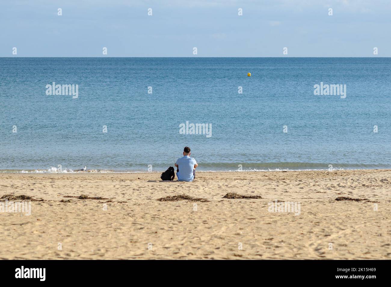 Bournemouth, Dorset, England, UK, 15th September 2022, Weather. All is quiet on the beach during the afternoon in early autumn sunshine. A man sits alone at the water’s edge contemplating. Credit: Paul Biggins/Alamy Live News Stock Photo