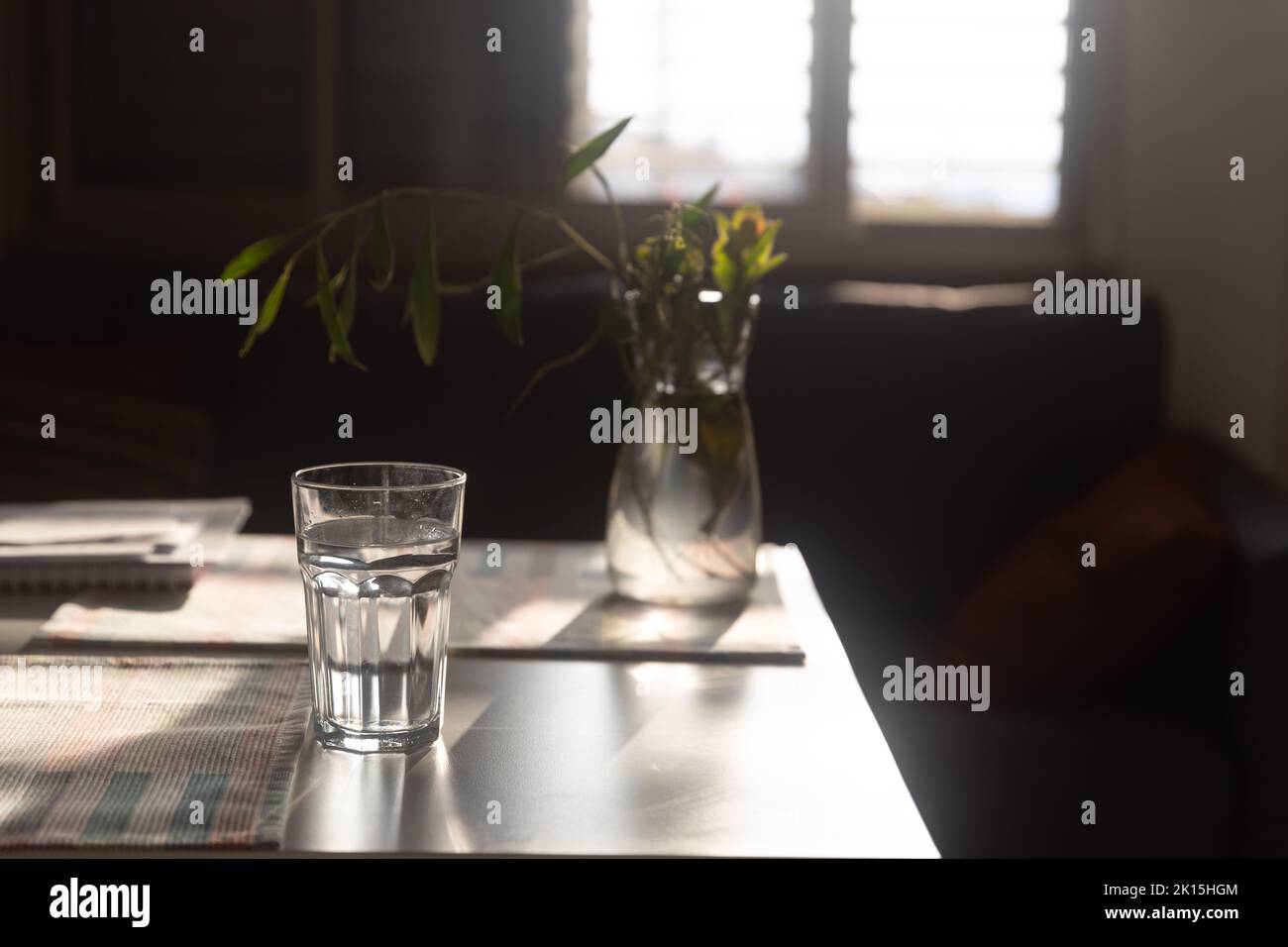 A glass of water and a bottle in the background against a backlit window with jalousie Stock Photo