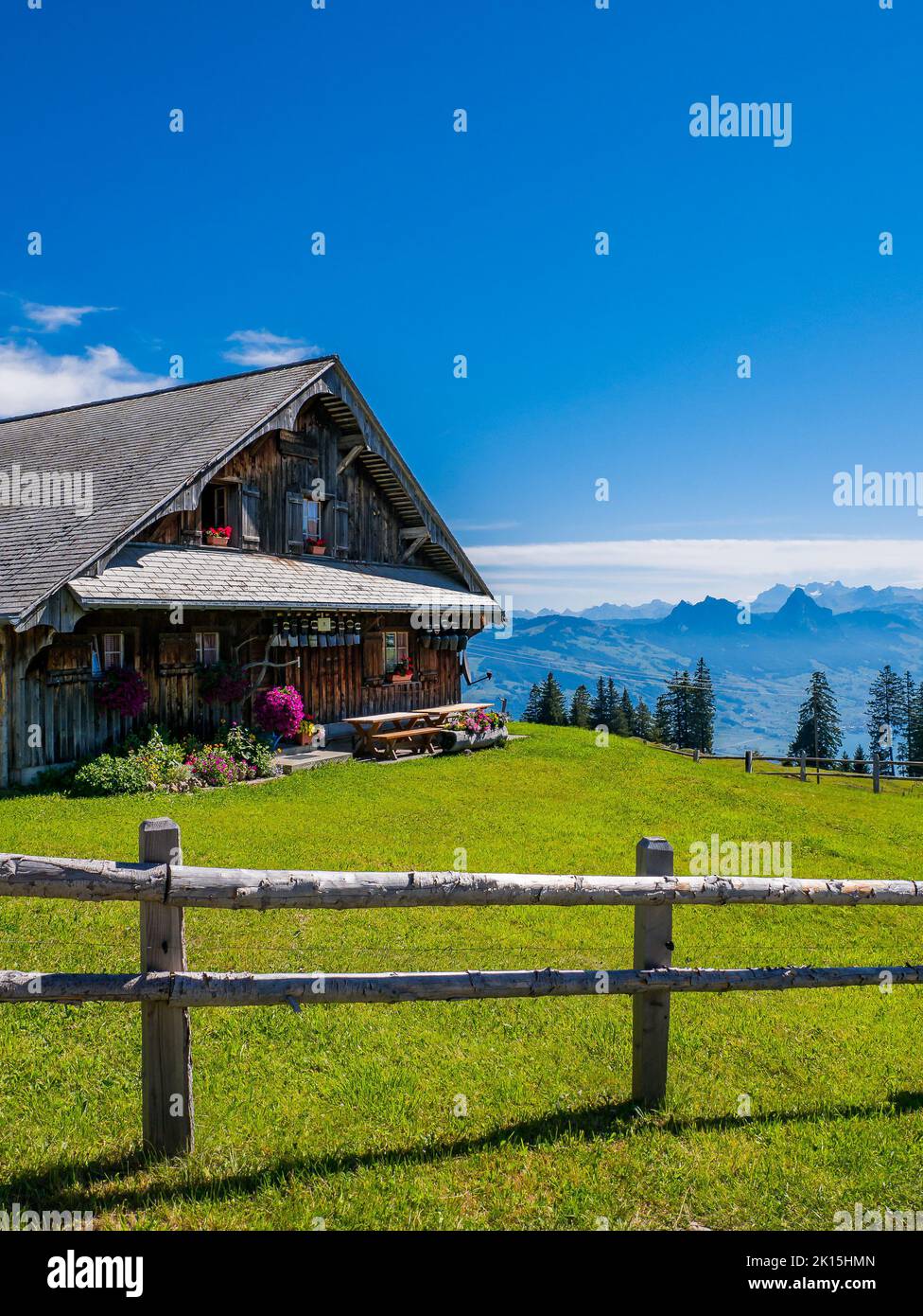 A beautiful wooden cottage on a mountain meadow in Switzerland with flowers in the windows. Stock Photo