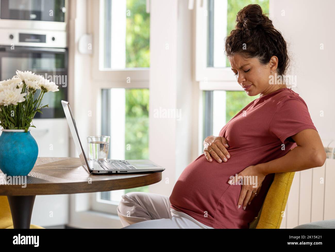 Pregnant woman sitting on chair in table with laptop in front of her and having back pain after overwork Stock Photo