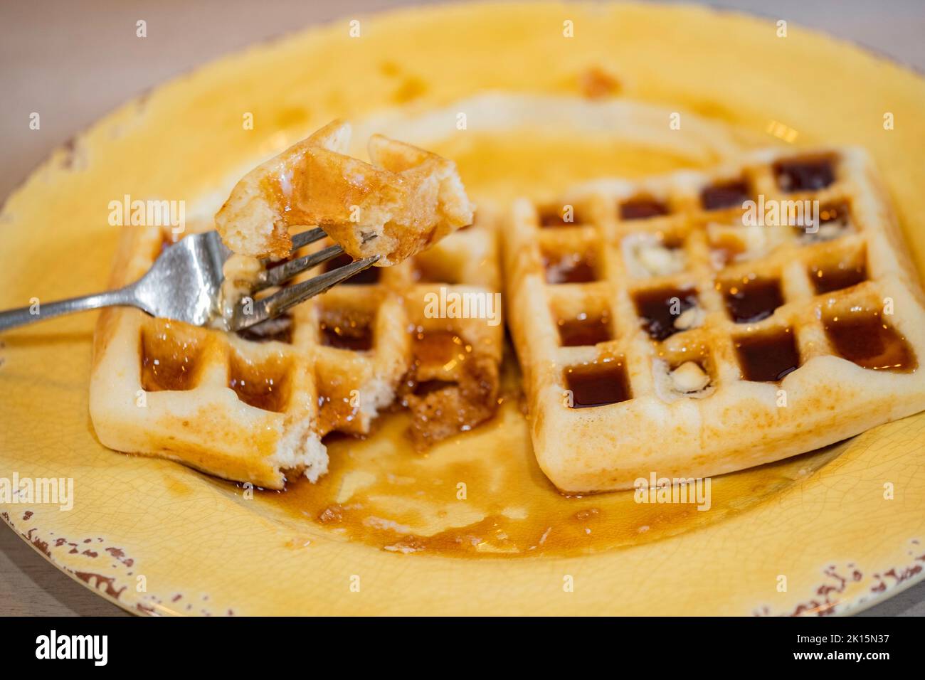 Homemade waffles smothered in maple syrup for breakfast. Yellow plate. USA. Stock Photo