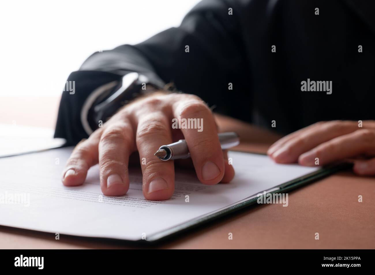 Low angle closeup view of a businessman holding a pen proofreading a contract or document in a folder. Stock Photo