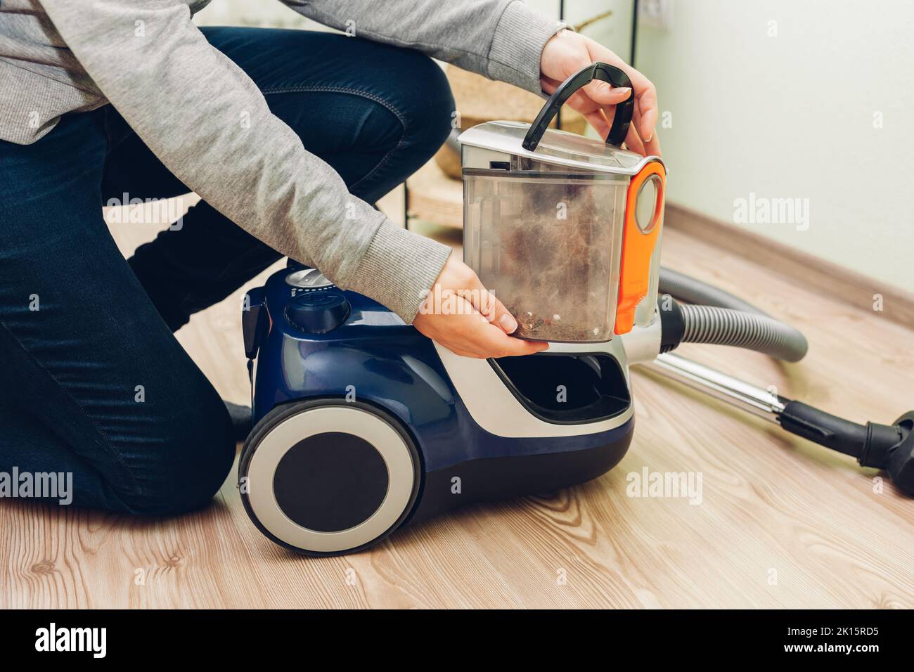 Woman takes container with dust filter out of canister vacuum cleaner