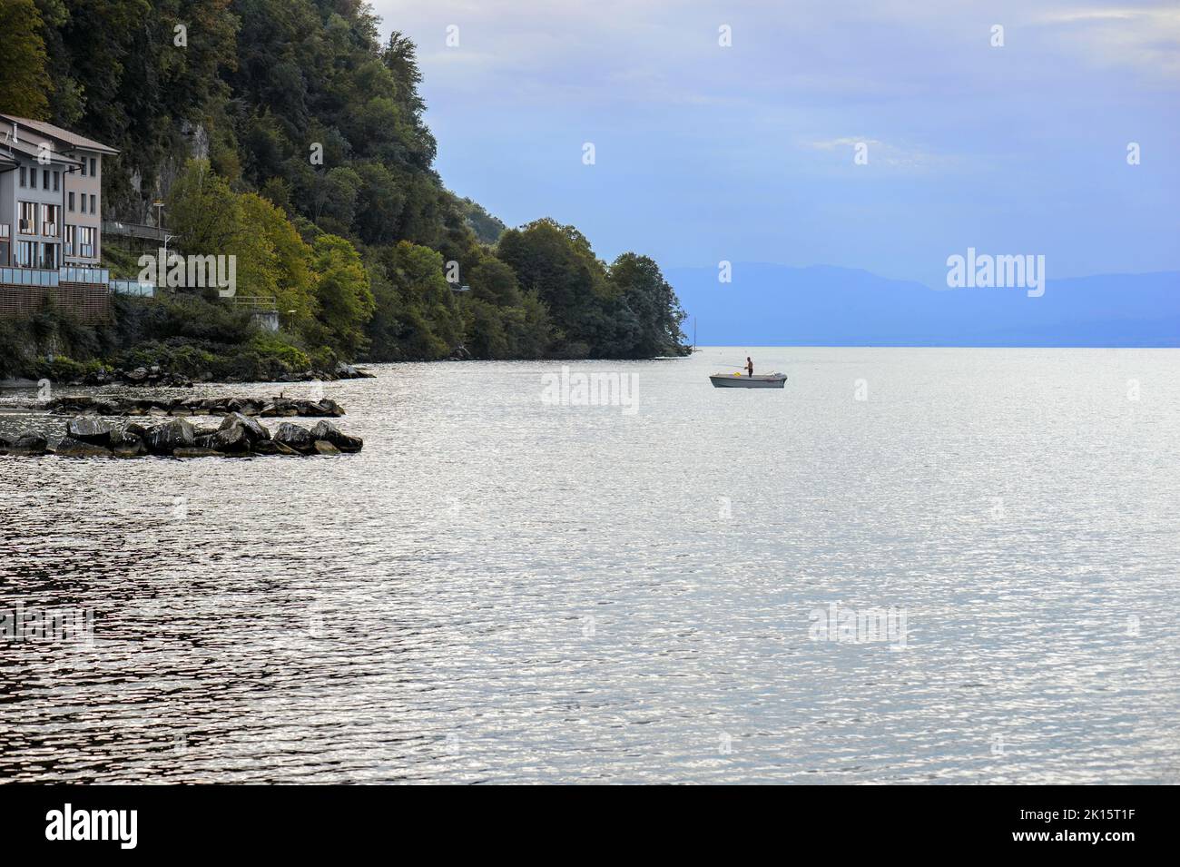Fisherman in a boat, in the evening on the calm waters of Lake Geneva. Silhouette in backlight of a fisherman and his boat in front of the mountain; Stock Photo