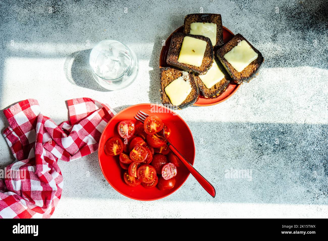 From above summer salad of ripe red cherry tomatoes in the bowl and toasts with melted cheese on concrete background Stock Photo