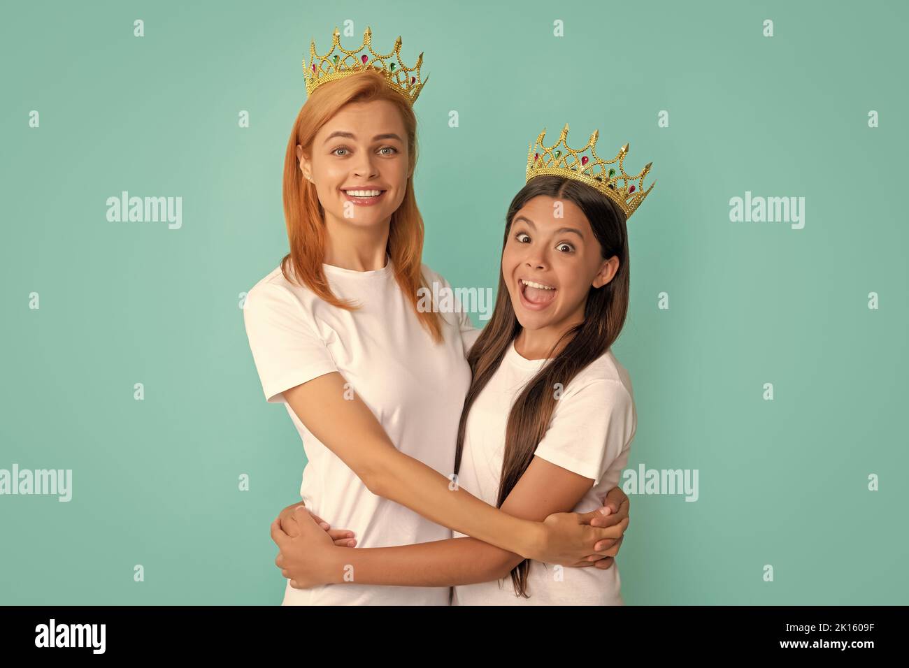 Happy woman and girl child in crowns hug smiling blue background, mother Stock Photo